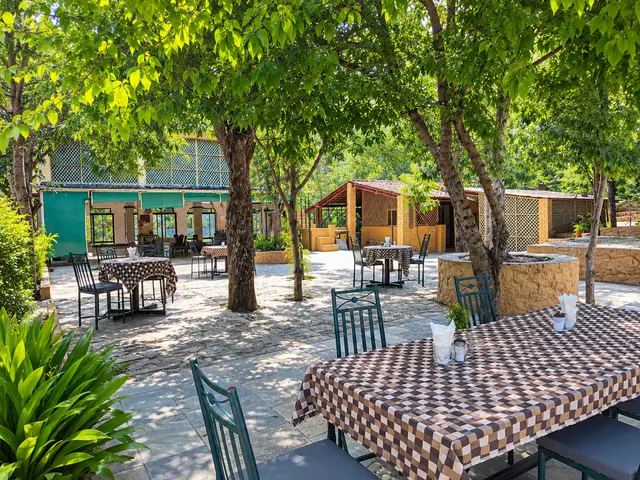 Open-air garden dining area with tables and chairs shaded by trees on a stone-paved courtyard