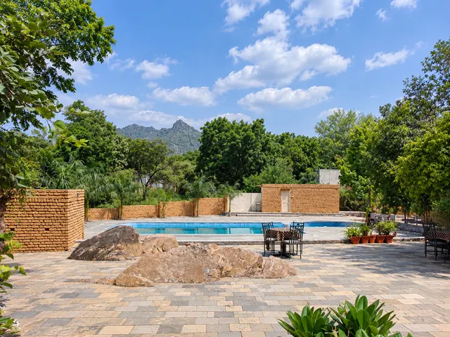 Paved terrace with natural boulders and outdoor tables beside the swimming pool, with a mountain peak in the distance