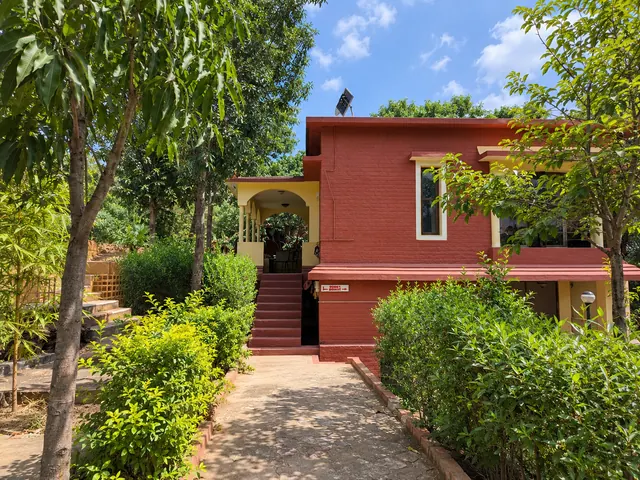 Red-painted brick house with an arched porch at the end of a stone garden path lined with shrubs