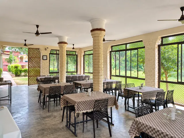 Covered dining hall at Roopam Resort with brick pillars, large windows and tables with checkered cloths overlooking the greenery