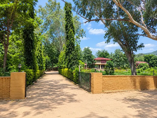 Tree-lined sandy path with a green gate and brick pillars leading to the red-roofed resort building