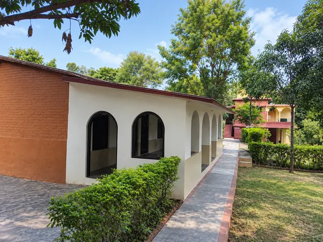 White building with arched windows and an orange brick wall beside a tiled garden path and trimmed hedges